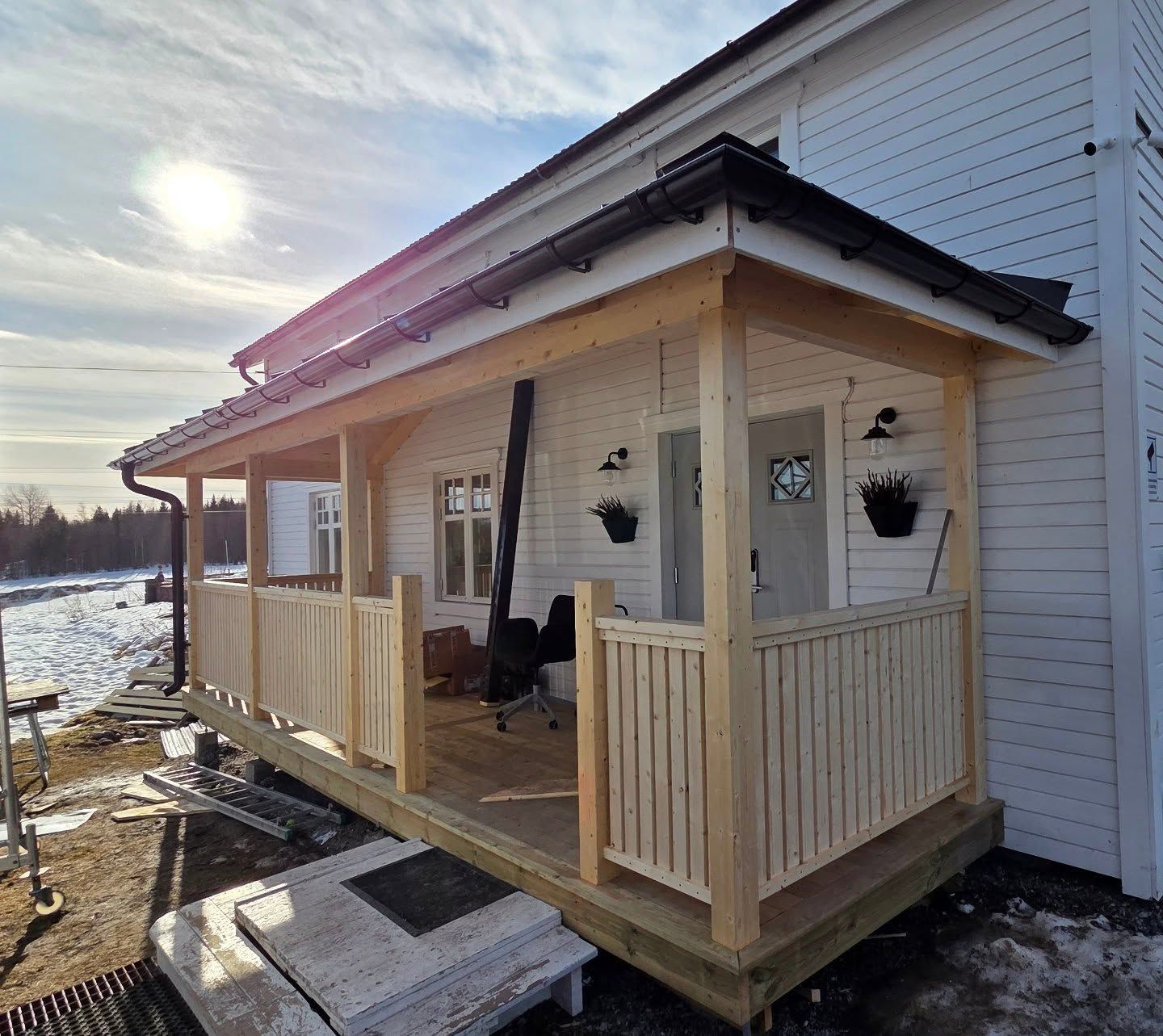 Nybyggd täckt veranda med vitt spjälräcke på ett vitt trähus